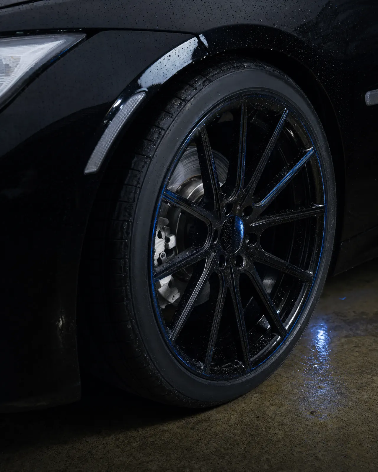 A glossy black wheel and dressed tire beaded with water